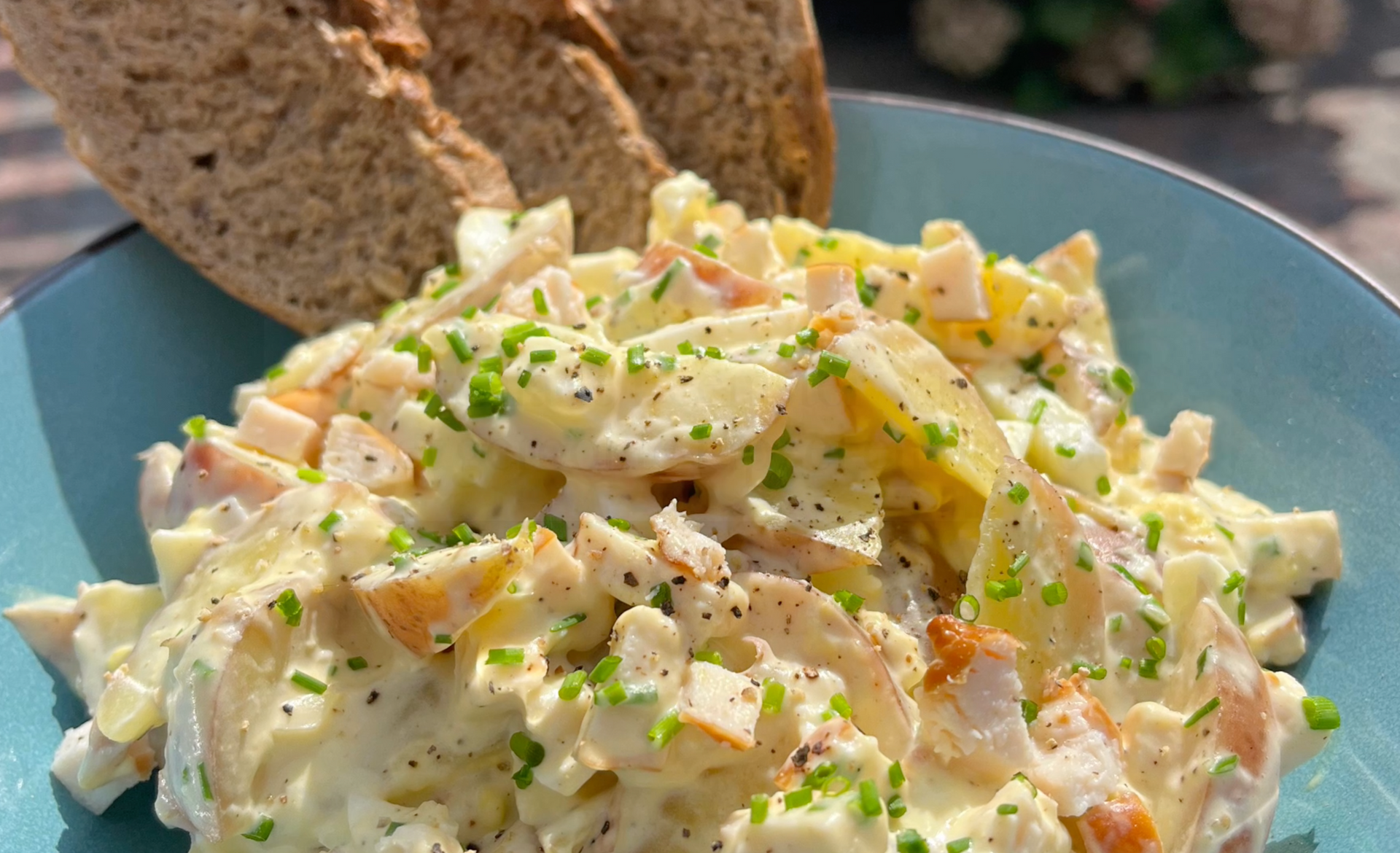 Romige kipsalade met peterseliegarnituur en sneetjes brood op een blauw bord.