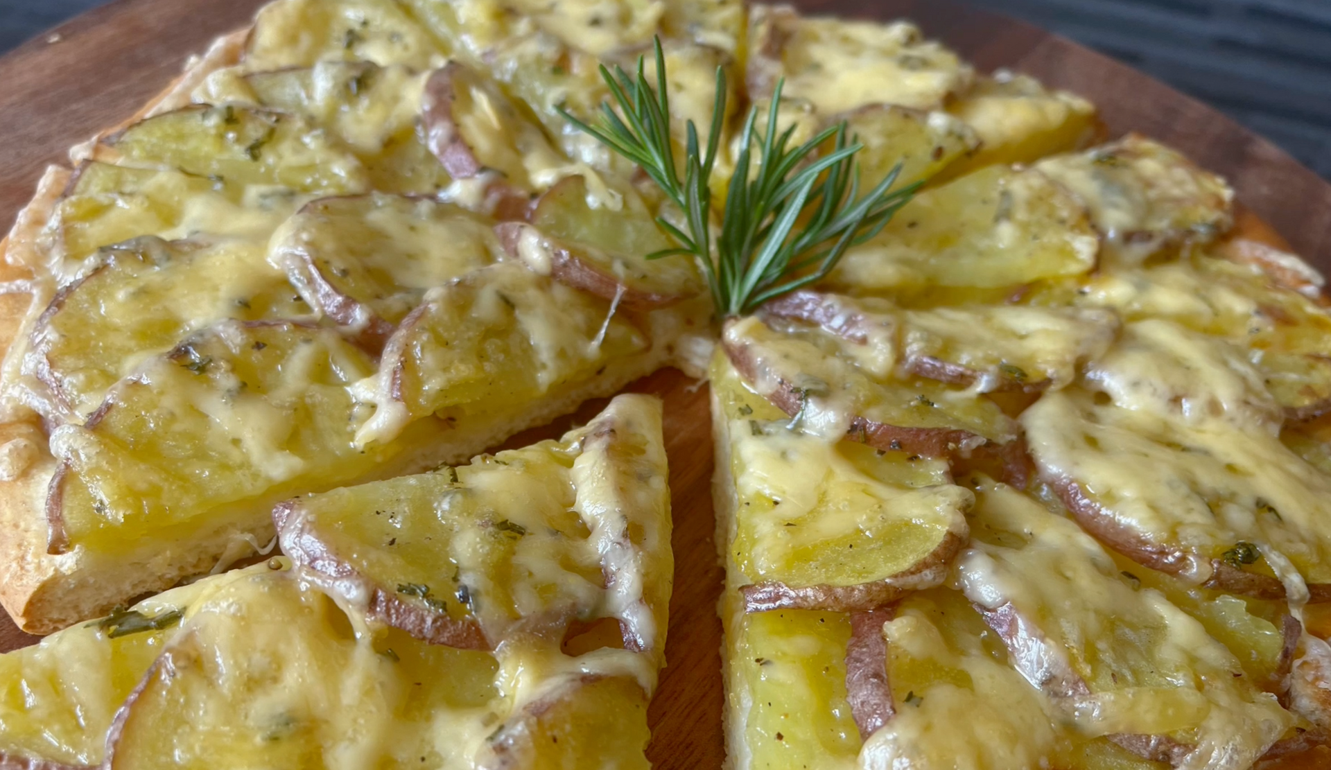 Gesneden aardappeltaart met kaas en rozemarijn, geserveerd op een houten plank.