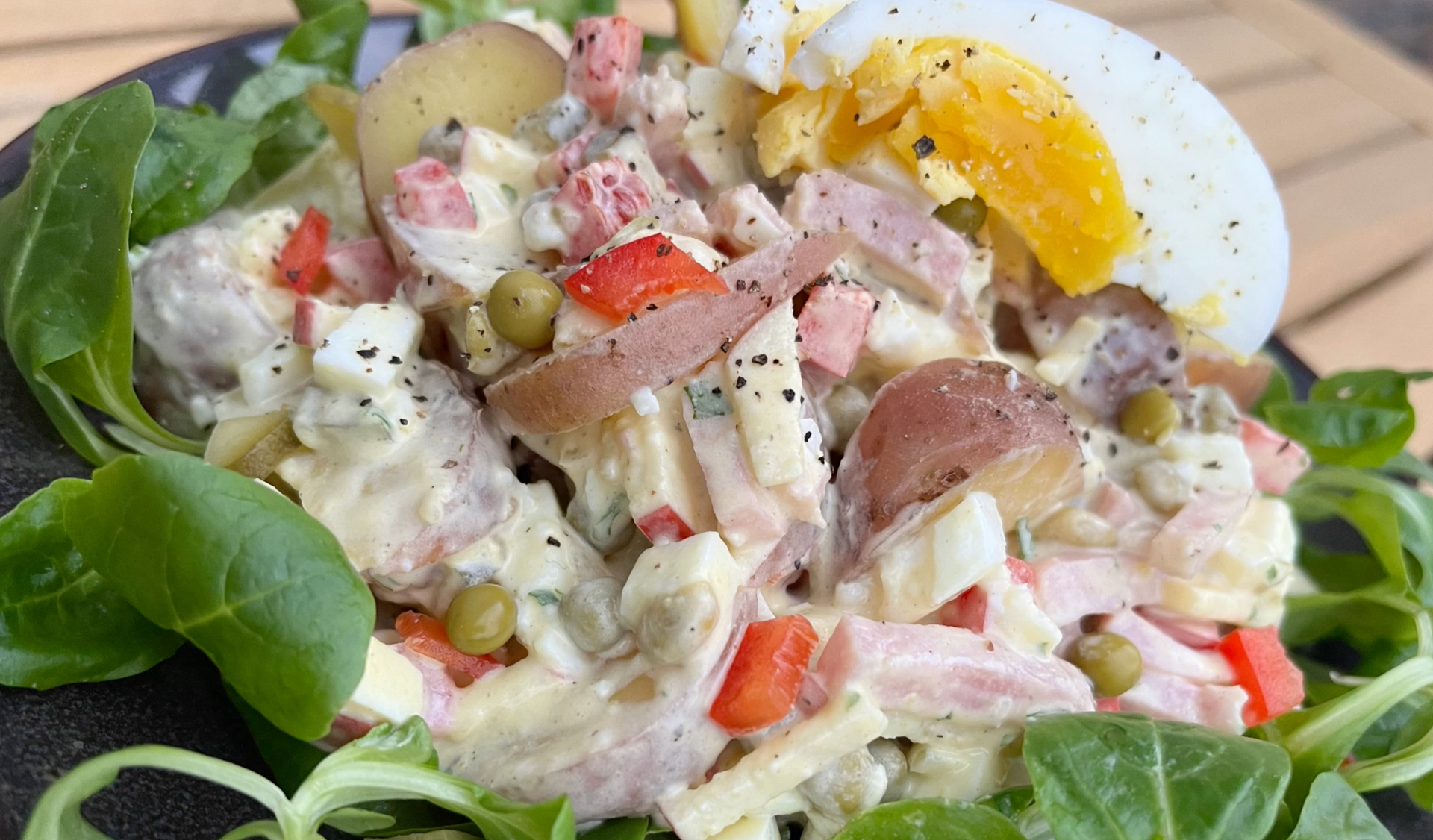 Tonijnsalade met aardappelen, in blokjes gesneden groenten en een half gekookt ei op bladgroenten.