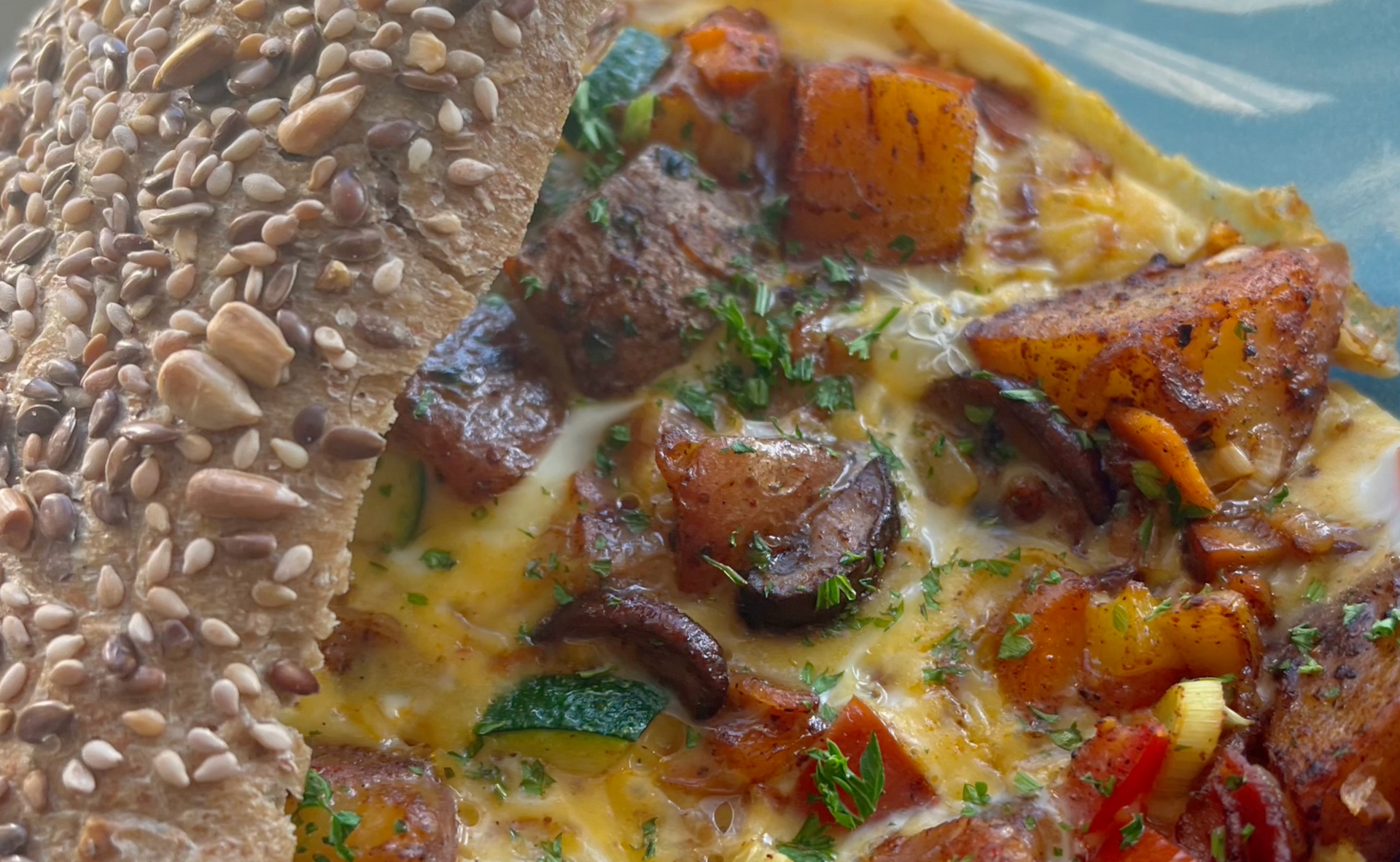 Close-up van een sesambroodje met een zichtbare vulling van groenteomelet en kruiden.