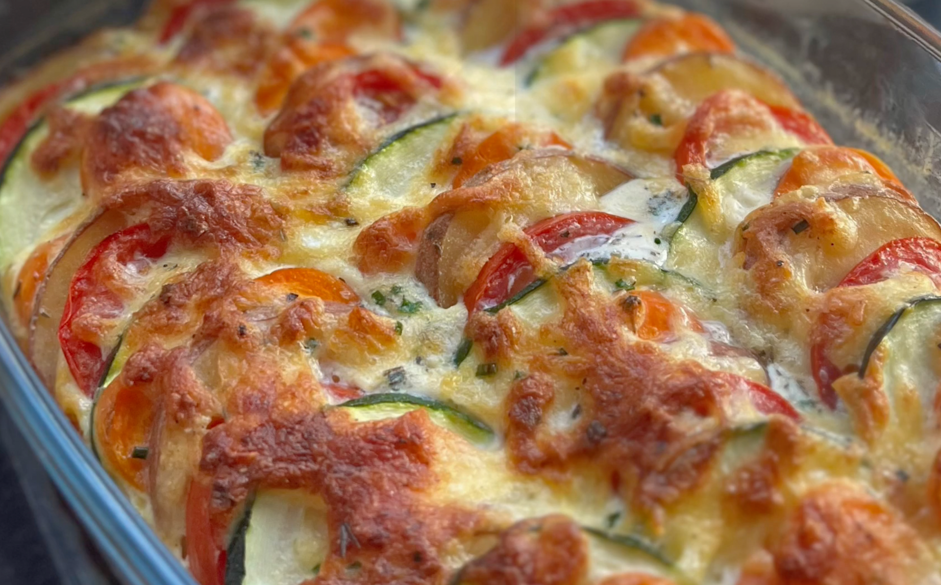 Gebakken groenteschotel met gesmolten kaas, met plakjes tomaat, courgette en aubergine.