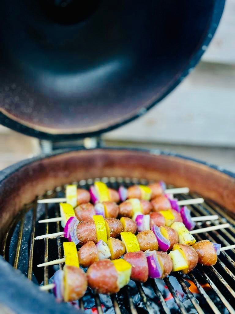Kleurrijke spiesjes die op de barbecue worden gegrild, met het deksel open en gloeiende houtskool eronder.