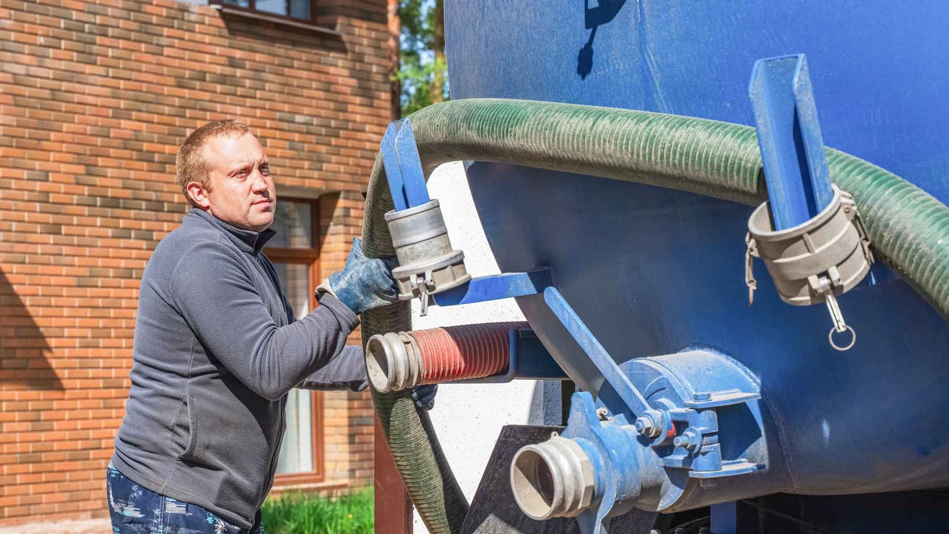 A technician is inspecting an open septic tank with a pump truck hose attached nearby. A technician is inspecting an open septic tank with a pump truck hose attached nearby.