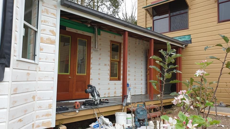 Partially renovated house exterior with white siding, wood-framed doors, and a covered porch