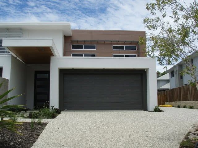 Modern two-story house with a white facade, dark garage door, and sloped driveway