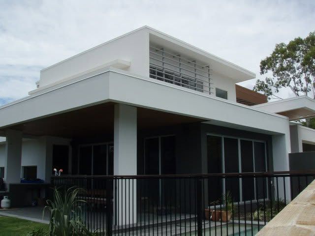 Modern white house with large windows, dark lower level, and black fence in front