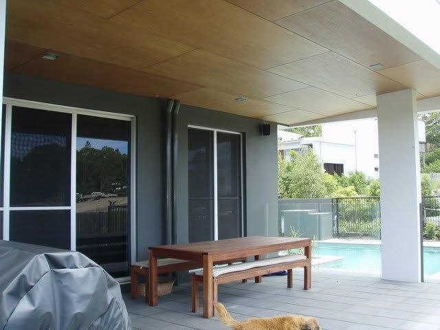 Covered patio with wooden table and benches beside a pool and sliding glass doors