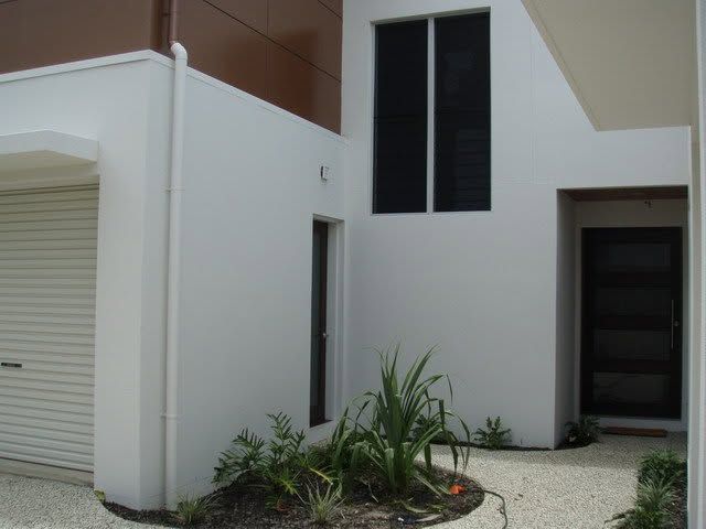 Modern white house exterior with garage, dark windows, and a small front garden