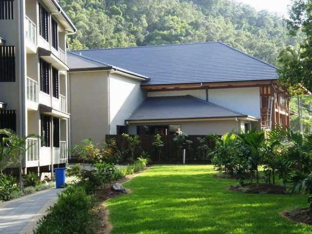 Courtyard between apartment buildings with green lawn, shrubs, and a wooded hillside in the background