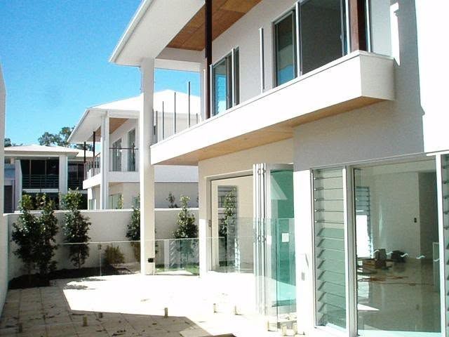 Modern white apartment buildings with balconies and glass doors under a clear blue sky