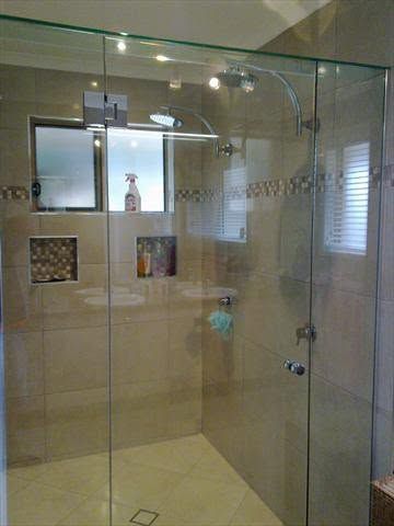 Glass-enclosed shower with beige tile, built-in shelves, and a chrome showerhead and door handle.