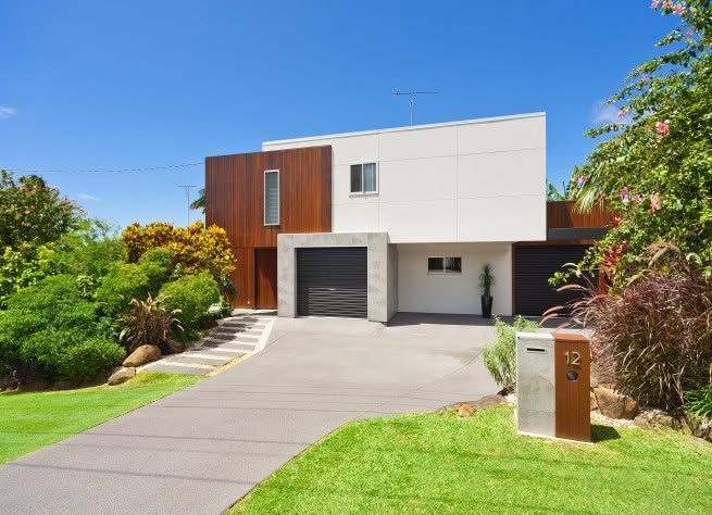 Modern two-story house with driveway, garage, and lush front yard under a blue sky