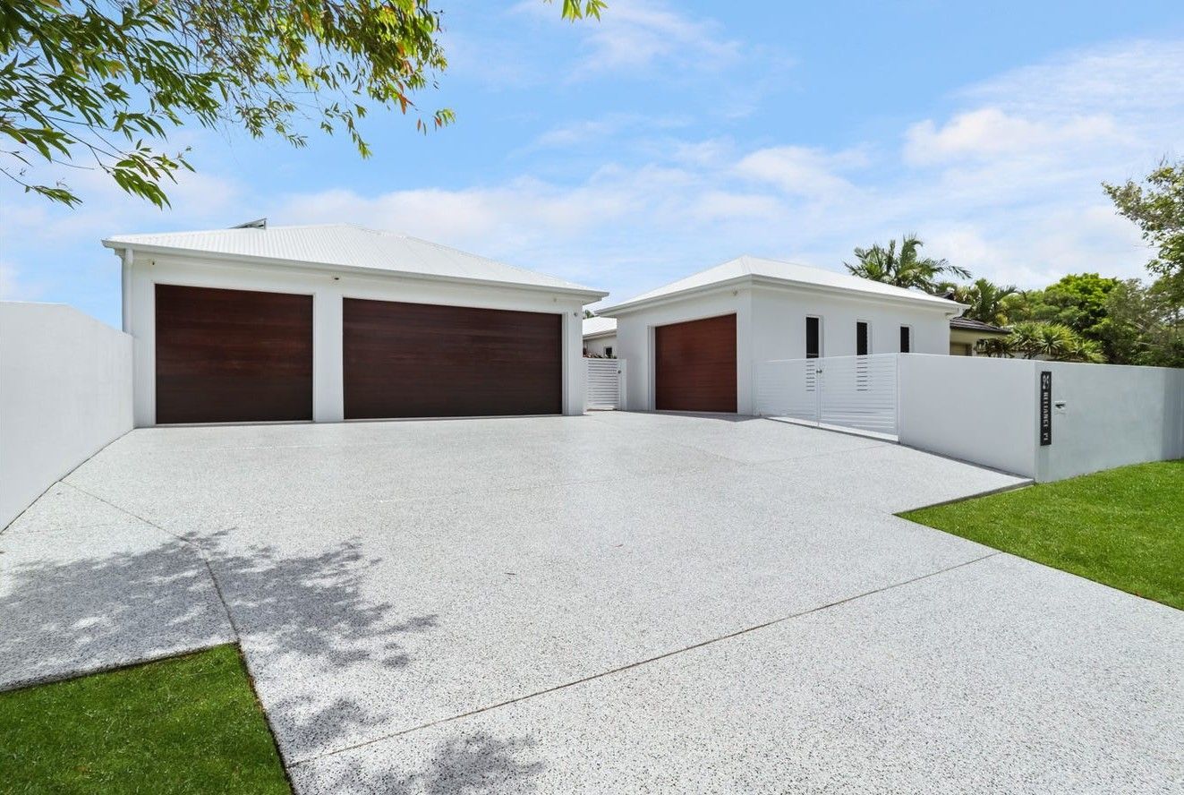 Modern white house with a large driveway, double garage doors, and green lawn under a blue sky