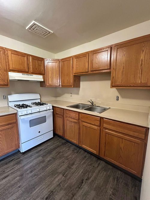 Kitchen with light brown wooden cabinets, a white stove, a double sink, beige countertops, and gray wood-look flooring.