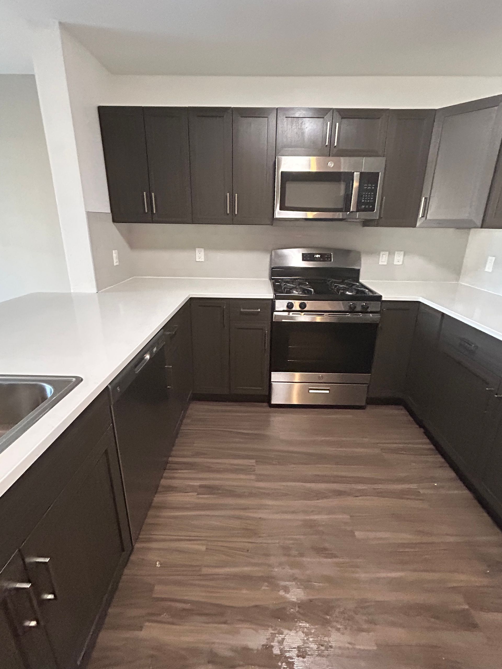 A modern U-shaped kitchen with dark brown cabinets, stainless steel appliances, and white countertops.