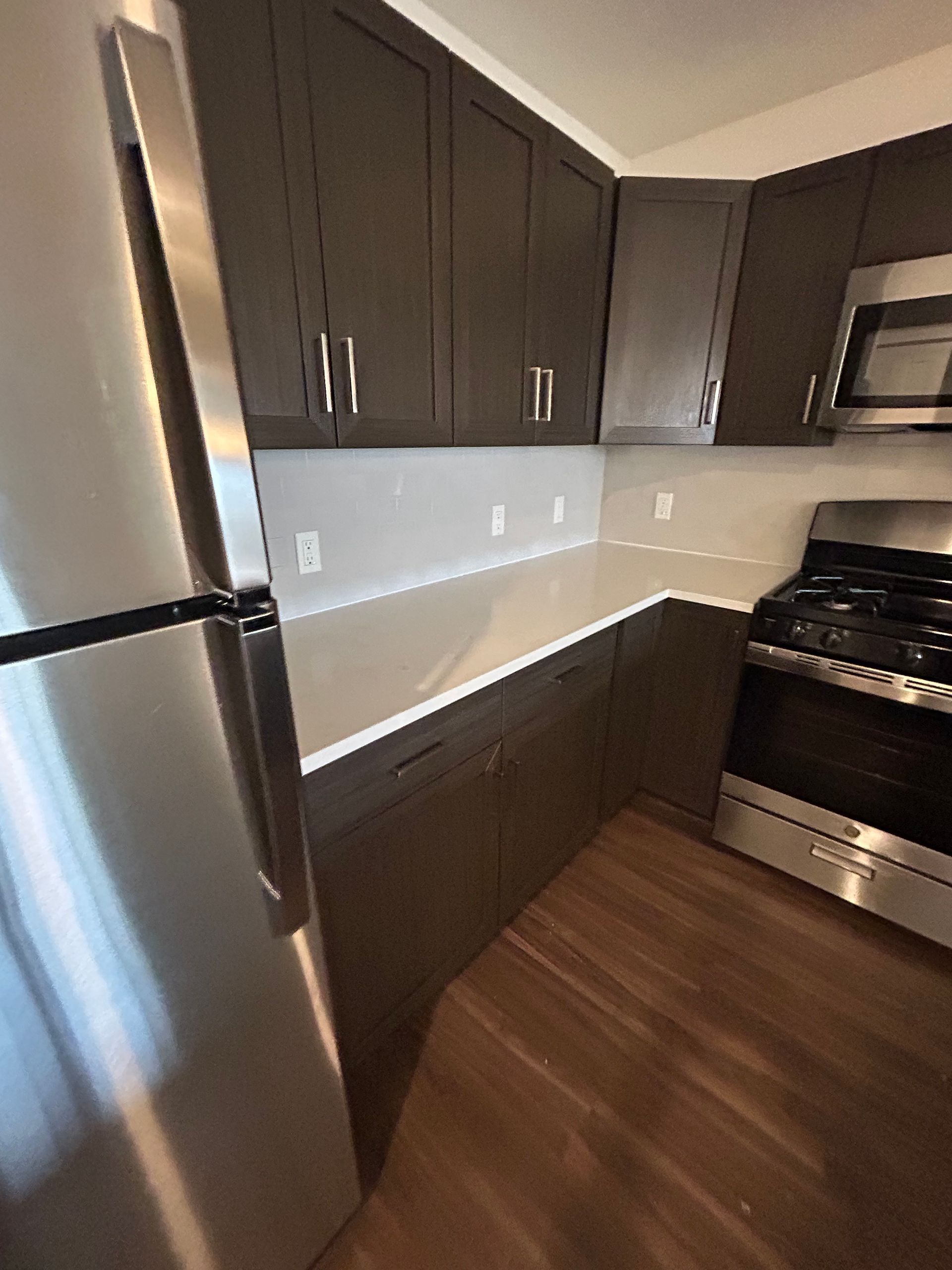 A modern kitchen with dark brown cabinets, a stainless steel refrigerator, white countertops, and a stainless steel stove.