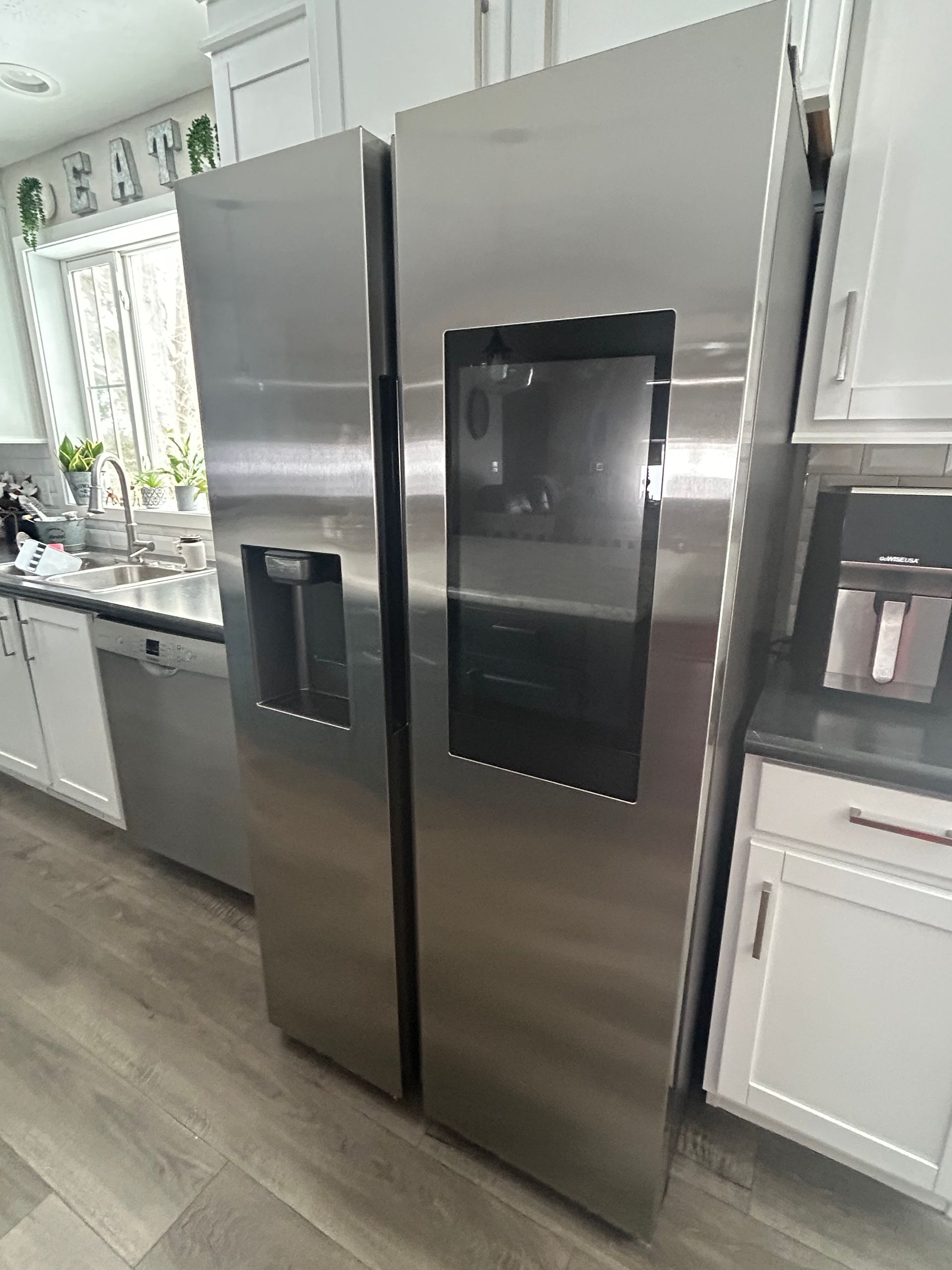 Stainless steel side-by-side refrigerator with a glass door panel and ice dispenser in a modern kitchen.