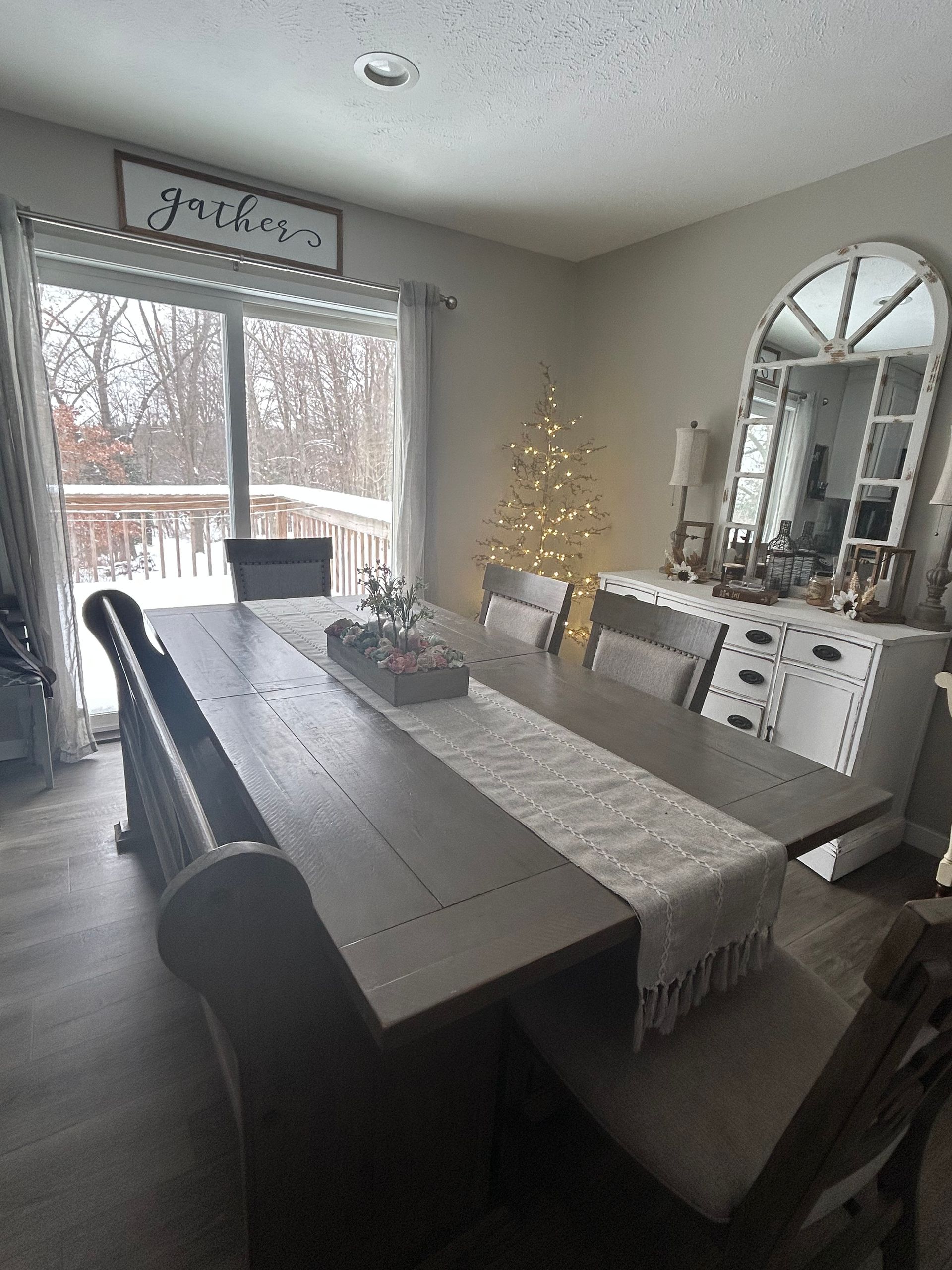 A dining room with a long wood table, a bench, and a light-colored runner, featuring a decorative mirror and winter decor.