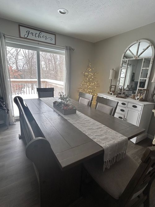 A dining room with a long wood table, a bench, and a light-colored runner, featuring a decorative mirror and winter decor.