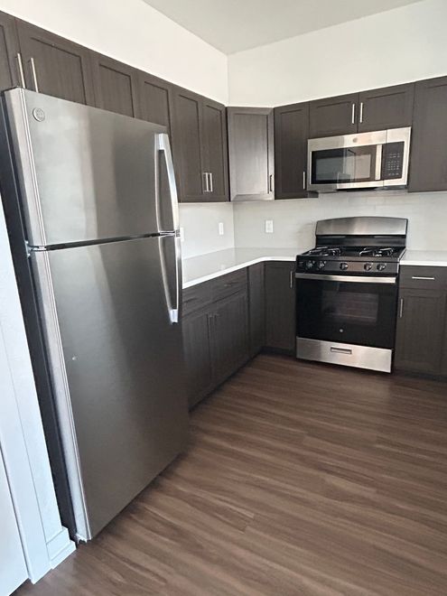 A modern kitchen with dark brown cabinets, stainless steel appliances, white countertops, and wood-patterned flooring.