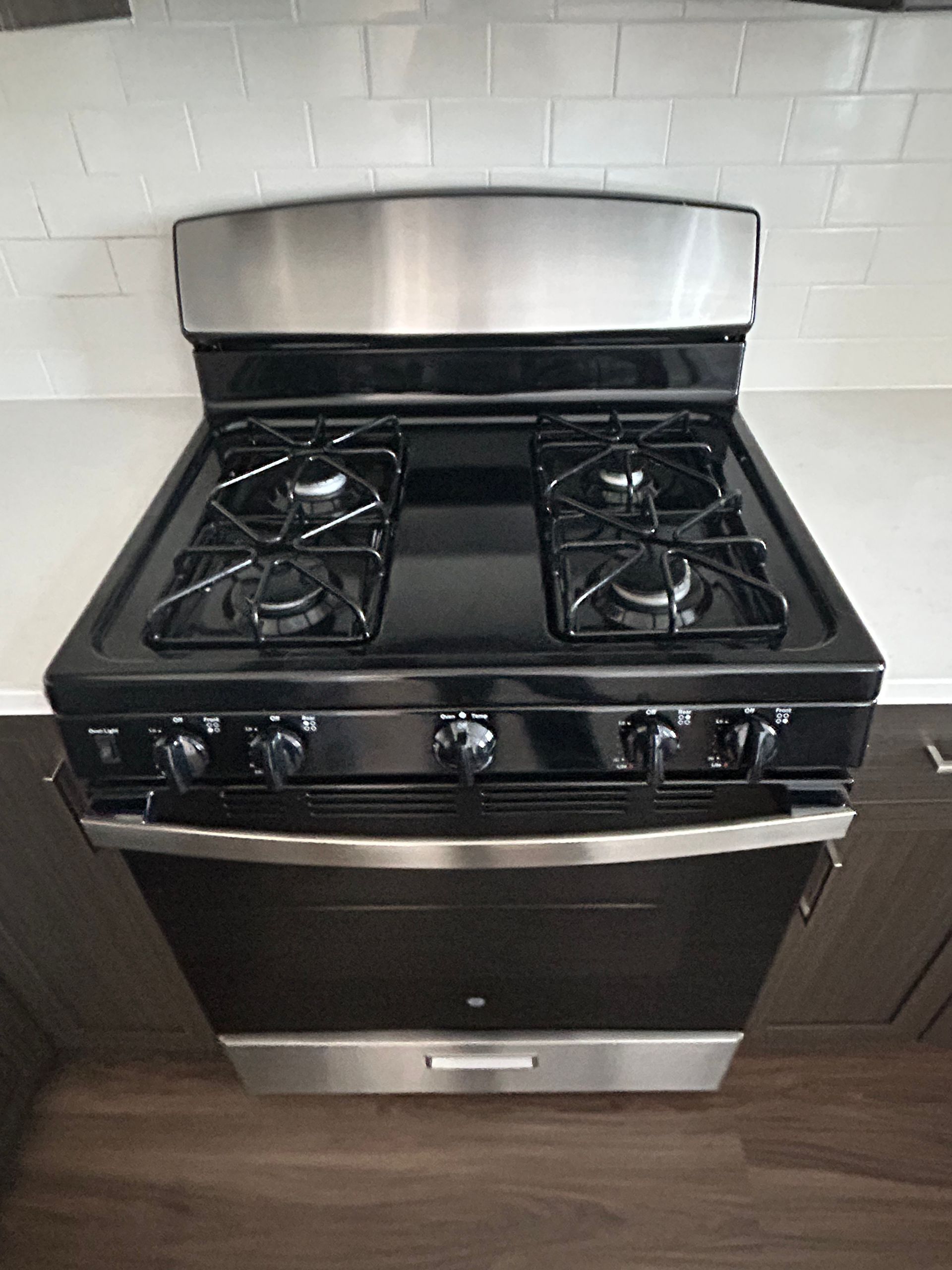 A black and stainless steel gas range with four burners, set against a white subway tile backsplash.