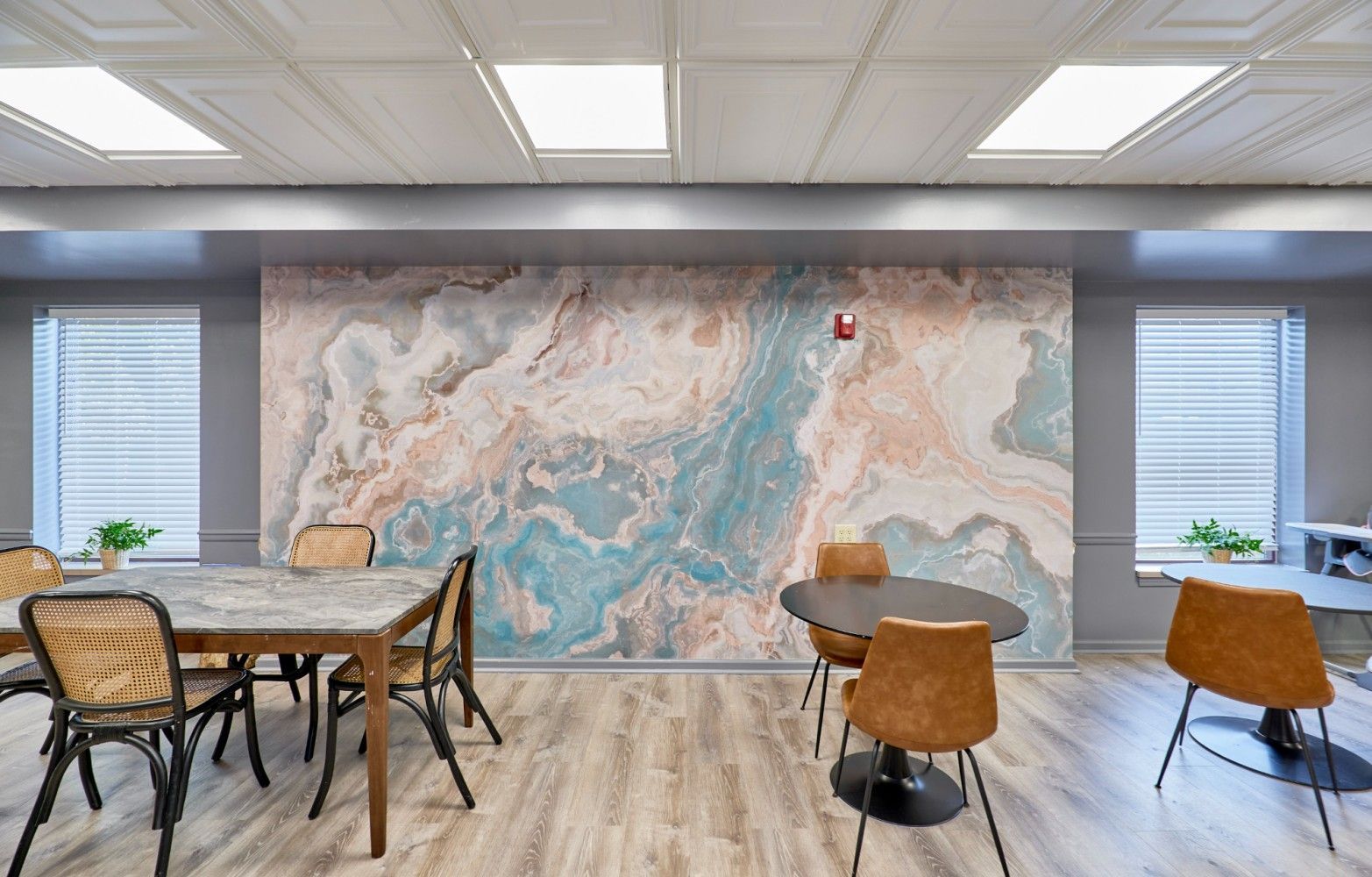 Modern conference room with a large abstract mural, wood tables, woven chairs, and bright windows