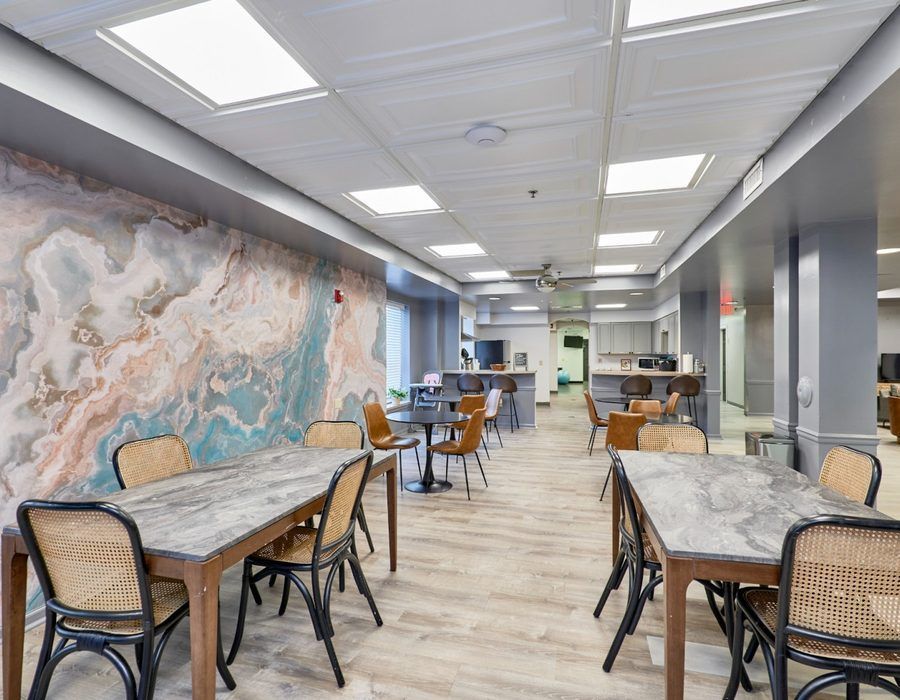 Modern cafe with marble-top tables, woven chairs, and a large abstract wall mural
