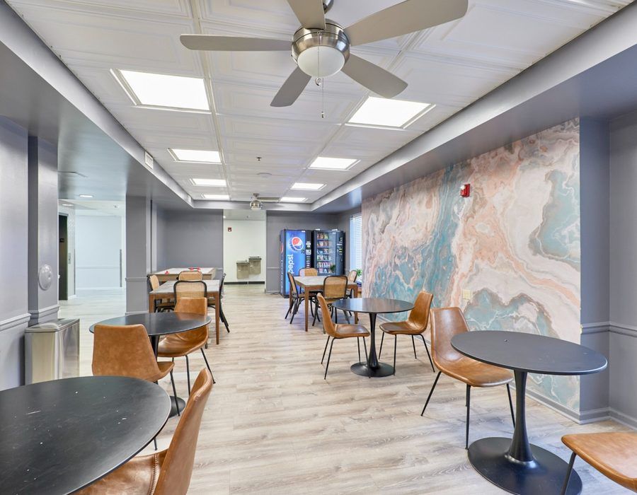 Modern café seating area with tables, chairs, ceiling fans, and a large abstract wall mural