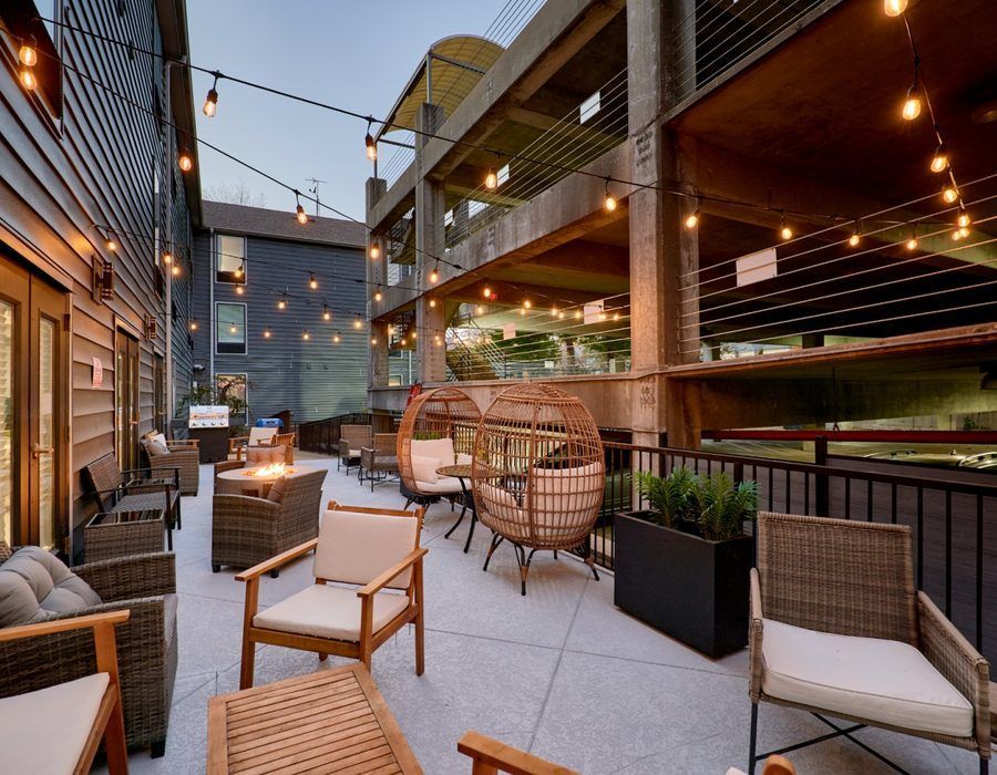 Outdoor rooftop patio with wicker seating, string lights, and planters beside a modern building