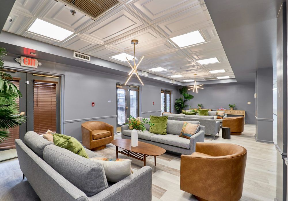 Modern lounge area with gray sofas, tan chairs, wooden tables, and bright ceiling lights
