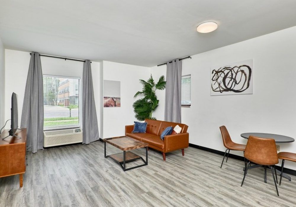 Modern living room with gray sofa, wooden desk, round table, and large windows.
