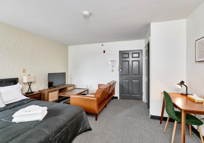 Motel room with two beds, sofa, desk, TV, and black door in a simple gray-and-white space