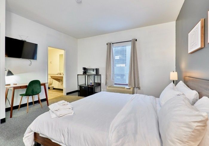 Bright bedroom with a bed, desk, wall-mounted TV, and window with curtains