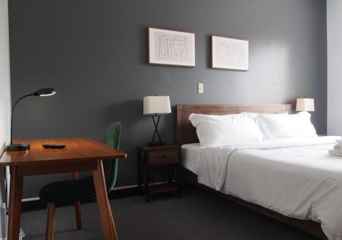 Minimal hotel room with a bed, desk, lamps, and gray walls