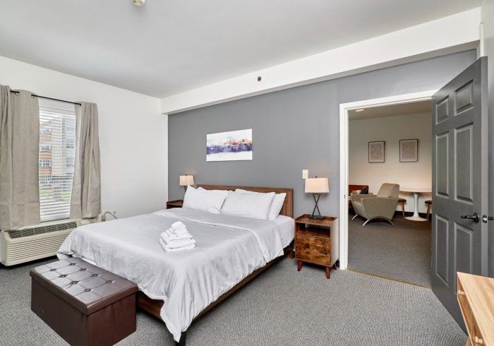 Bright bedroom with white bed, gray walls, bedside lamps, and an adjacent sitting area