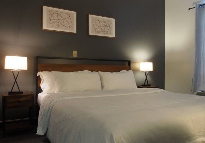Neatly made bed in a dim hotel room with bedside lamps and framed art above the headboard