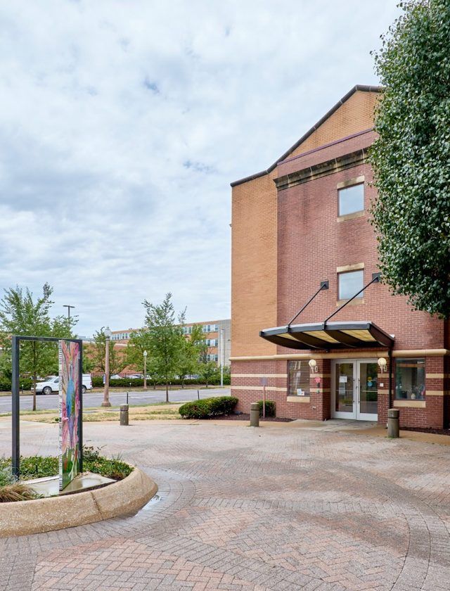 Brick apartment building entrance with a covered doorway and paved courtyard, lined with trees