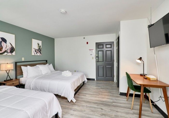 Modern hotel room with two white beds, desk, gray door, and wall-mounted TV