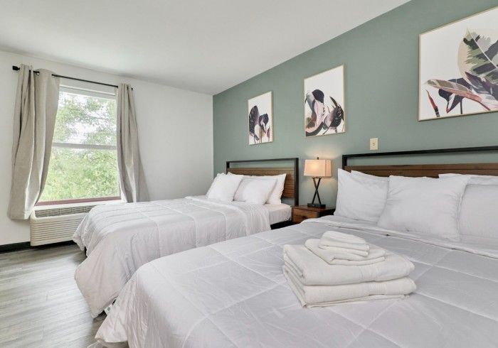 Bright bedroom with two white beds, teal accent wall, and window with curtains