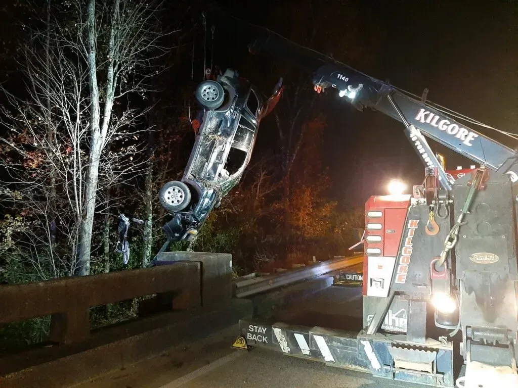 A car is being lifted over a bridge by a crane.