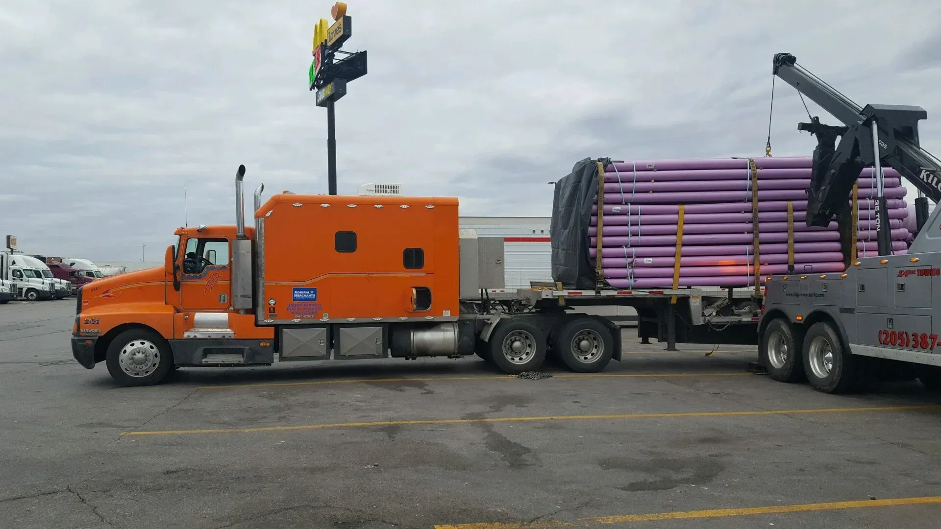 An orange semi truck is being towed by a tow truck in a parking lot.