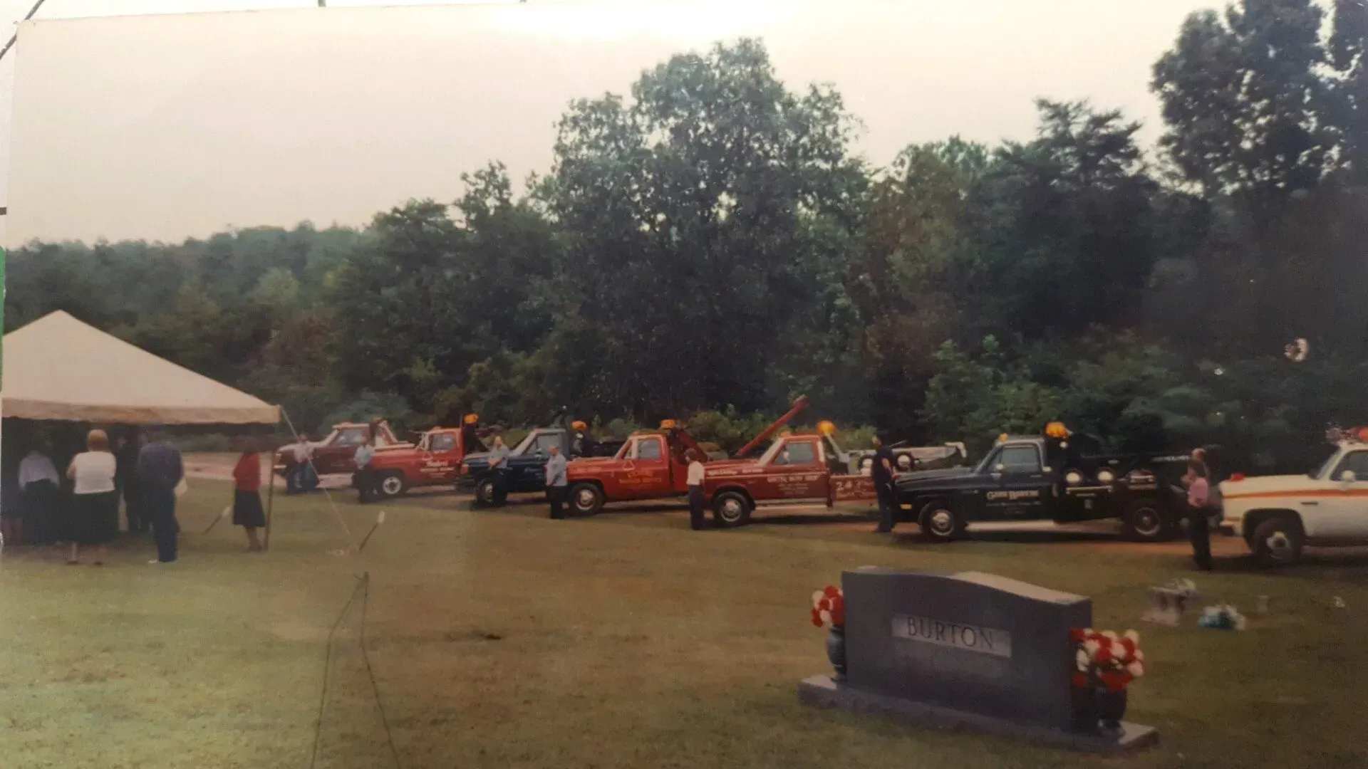A row of trucks are parked in a cemetery.