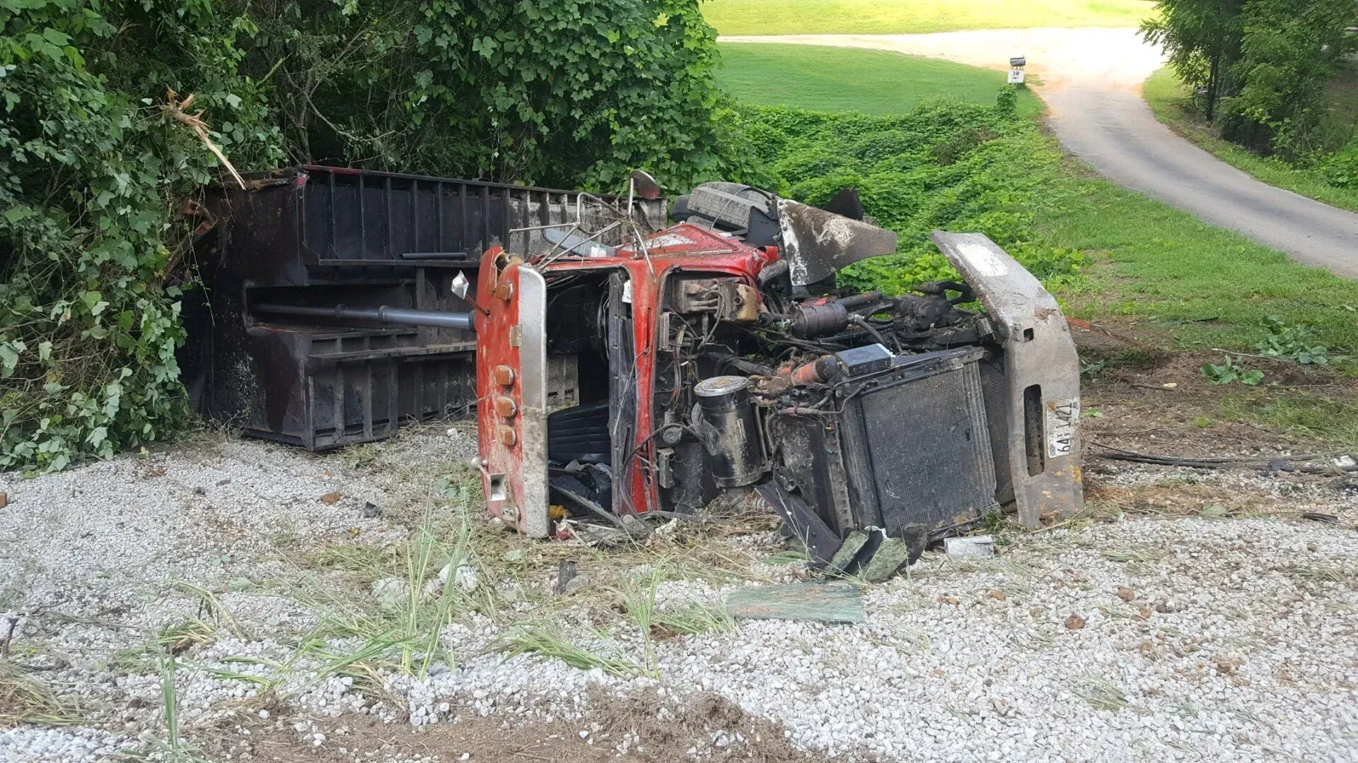 A truck is on its side in a gravel lot next to a road.