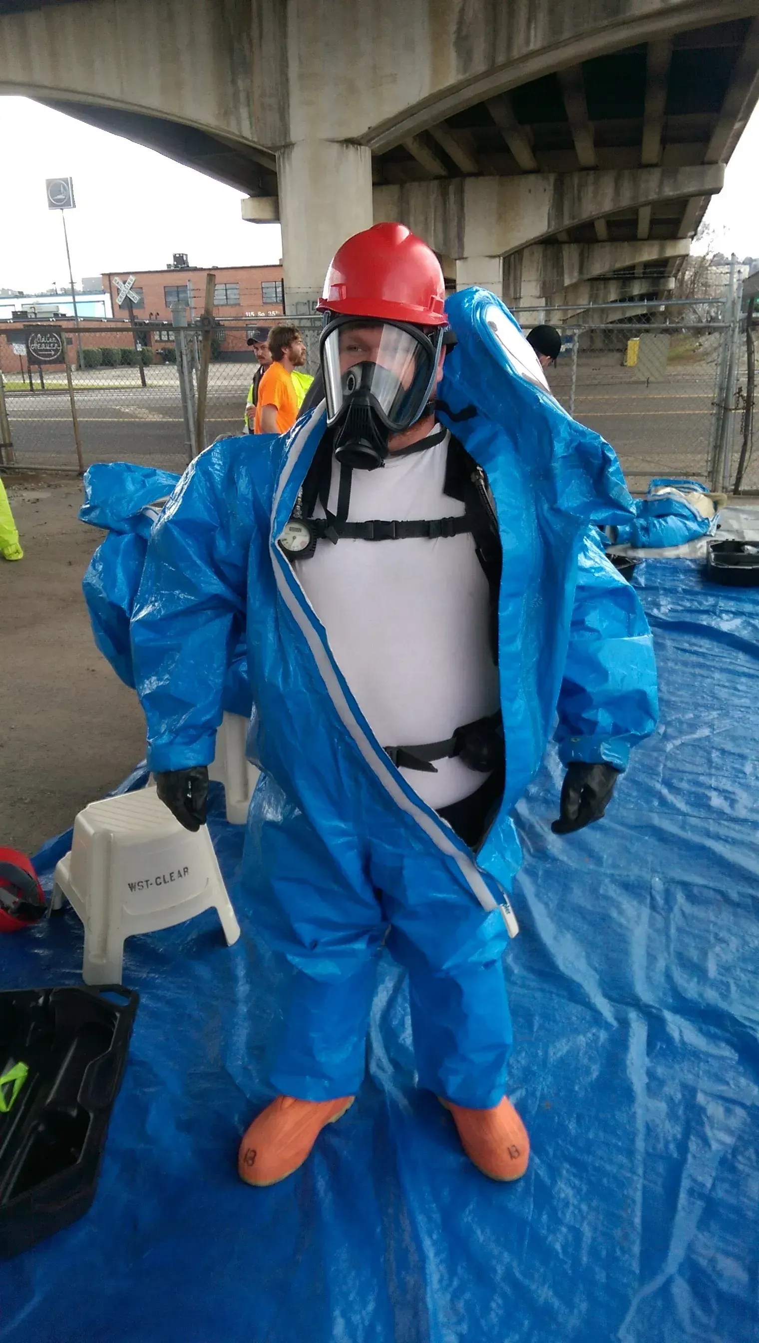 A man wearing a blue protective suit and a red helmet is standing on a blue tarp.