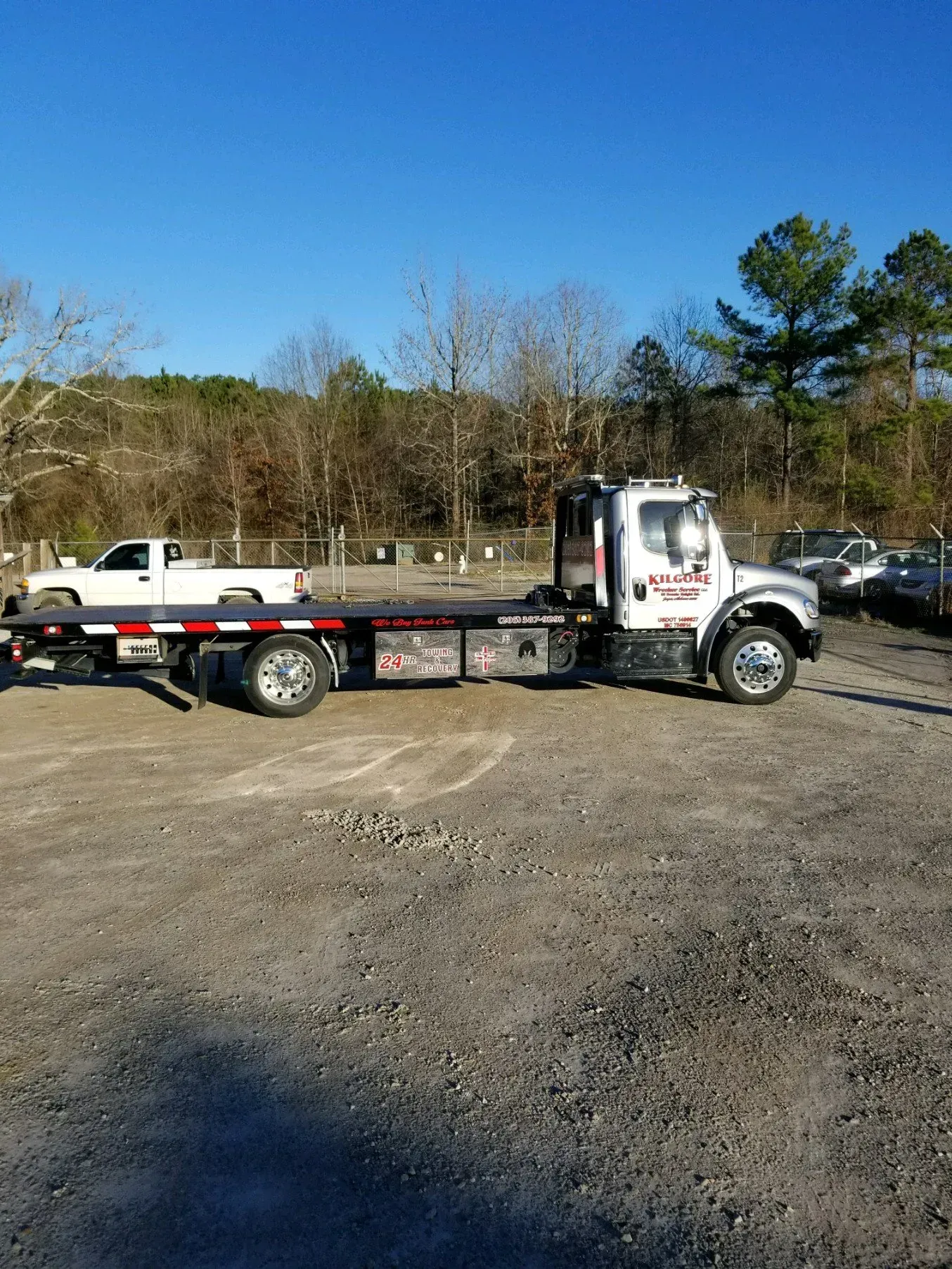 A tow truck is parked in a gravel lot next to a white truck.