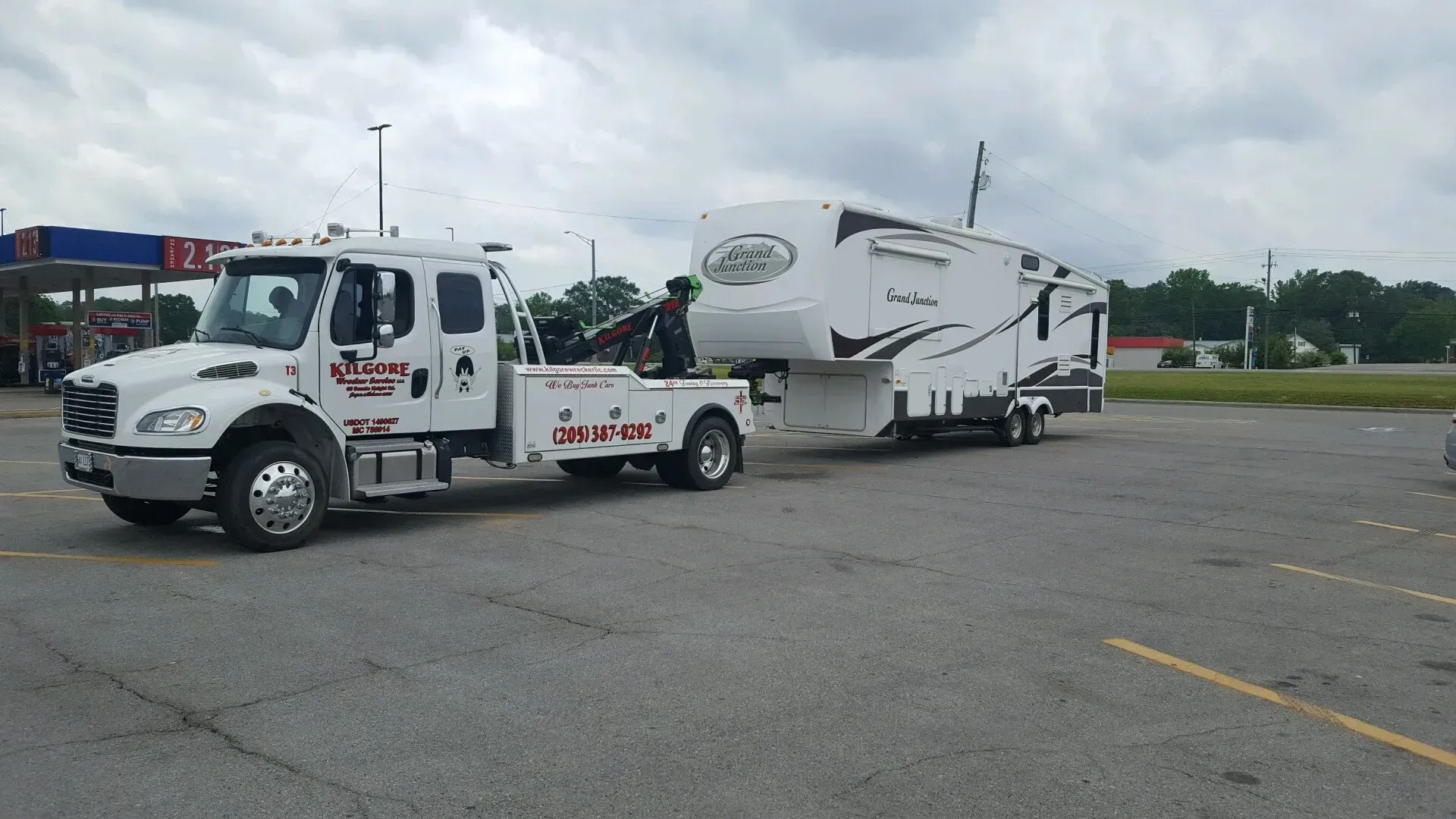 A tow truck is towing a rv in a parking lot.