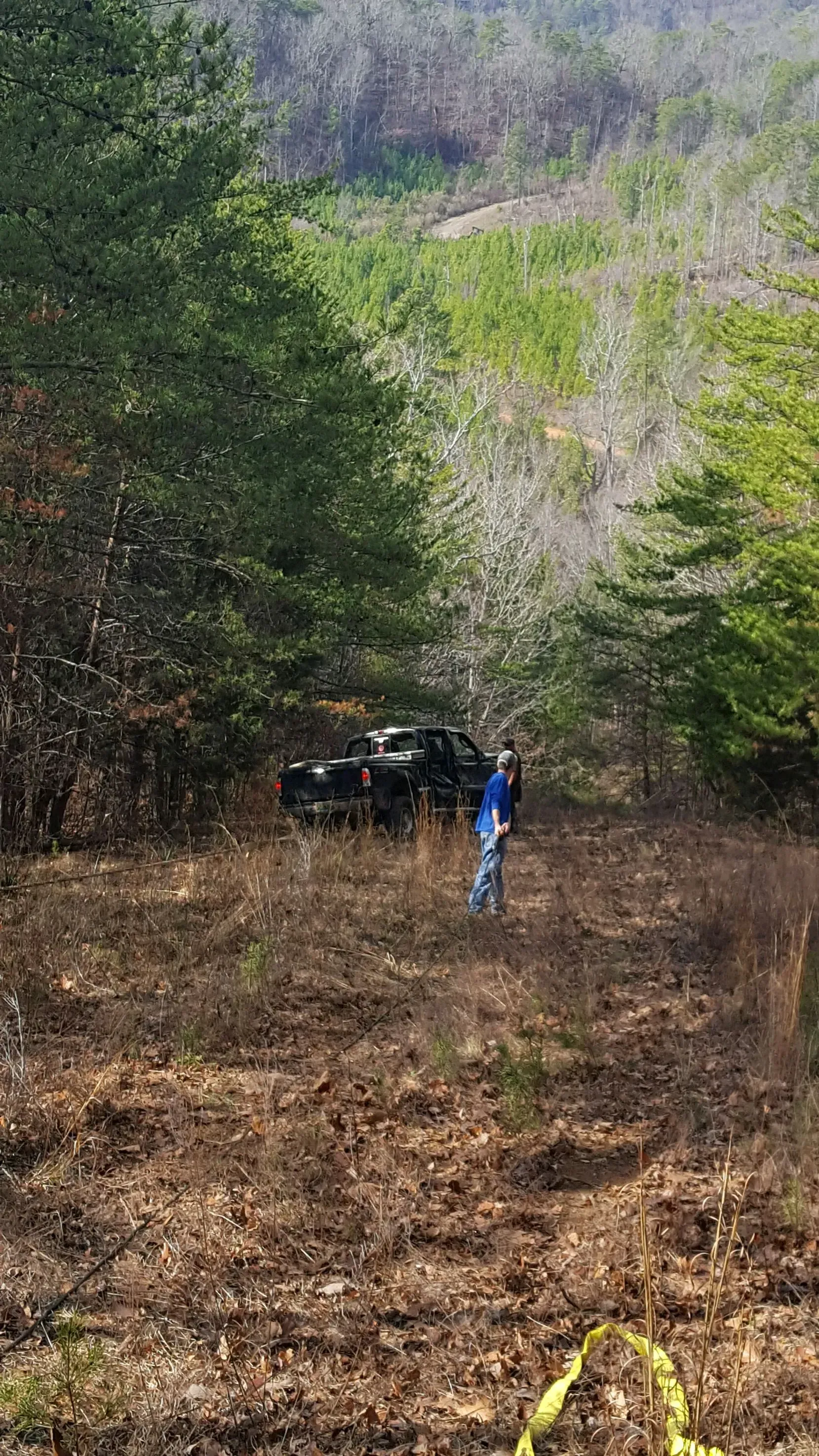 A man is standing in a field with a car in the background.