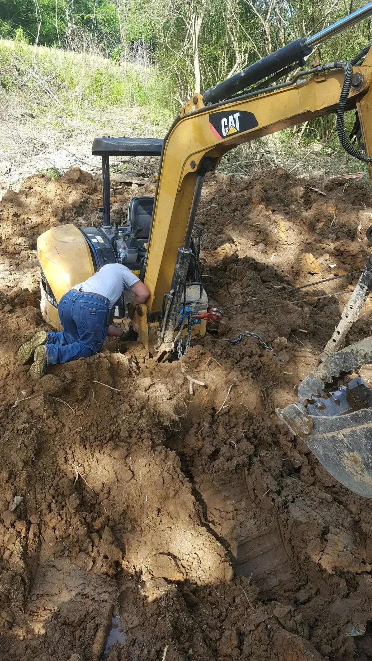 A man is kneeling in the dirt next to an excavator.