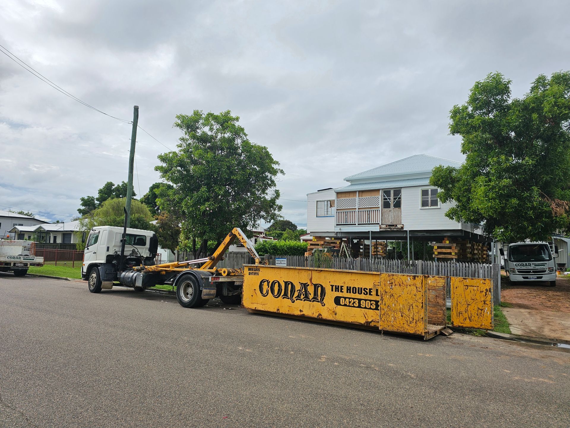 A Yellow Dumpster is Being Towed by a Truck in Front of a House — Conan The House Lifter In Townsville, QLD
