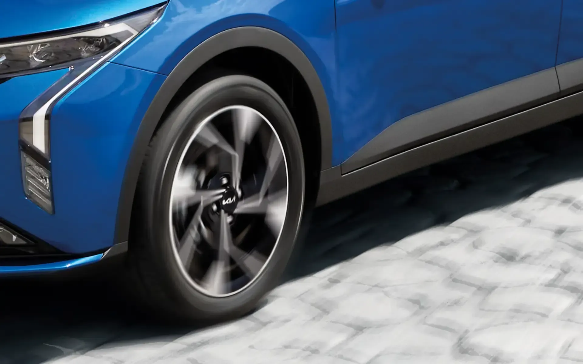 Rueda de SUV  kia k3 azul estacionada sobre un pavimento de piedra clara